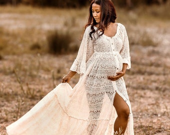 May include: A pregnant person in a white lace maxi dress with a long flowing skirt and a slit up the leg. The dress has a button-up front and a fitted bodice. The person is standing in a field of brown grass.