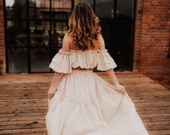 May include: A woman wearing a light beige off-the-shoulder top and a matching tiered maxi skirt. The skirt is flowing in the wind.