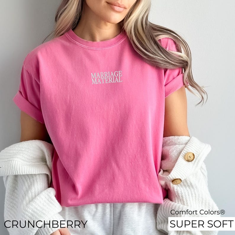 Puede incluir: Camiseta rosa de manga corta con el texto "Marriage Material" en letras blancas. La camiseta est&aacute; hecha de una tela suave y c&oacute;moda y tiene un corte holgado.