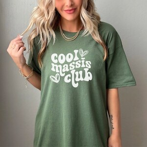 May include: A green t-shirt with the text "Cool Massis Club" in white with a heart design.