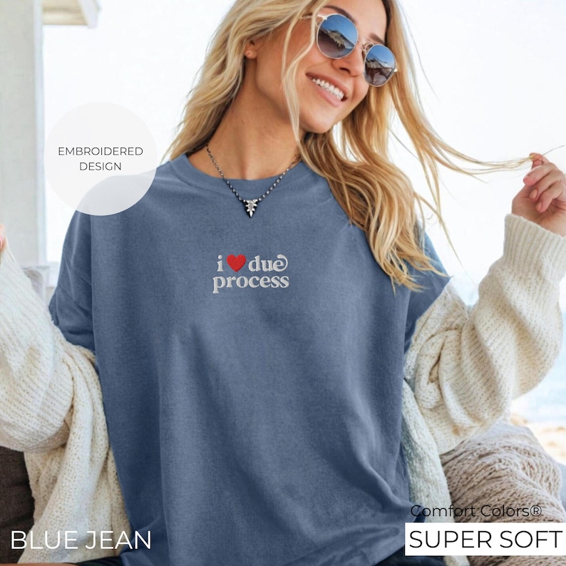 May include: Blue jean colored sweatshirt with the embroidered phrase "i ❤️ due process". The shirt is labeled "Comfort Colors Super Soft" and has the words "Embroidered Design" in a circle.