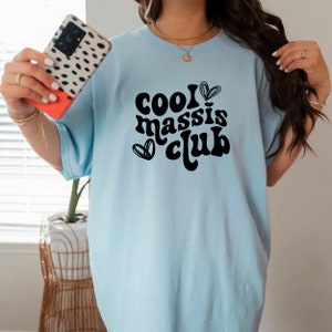 May include: A light blue t-shirt with the text "cool massis club" in black, with a heart graphic next to the word "cool".