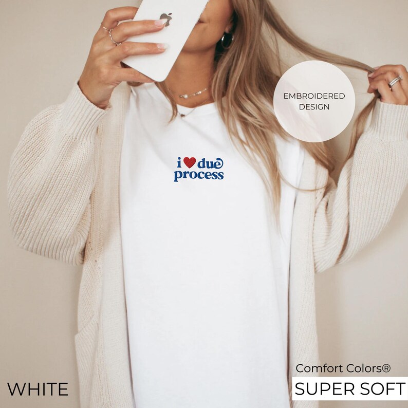 May include: White t-shirt with the phrase "i ❤️ due process" embroidered in red and blue. The shirt is labeled "Comfort Colors&reg; SUPER SOFT" and has a crew neck. The image also shows a cream-colored cardigan.