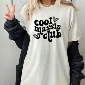 May include: White t-shirt with black text that reads "cool massis club" with two hearts on either side of the text.