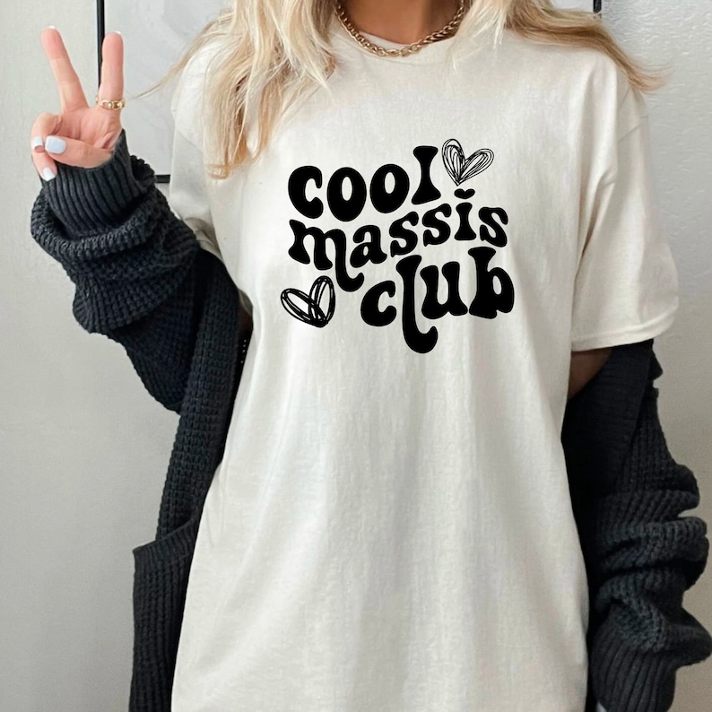 May include: White t-shirt with black text that reads "cool massis club" with two hearts on either side of the text.