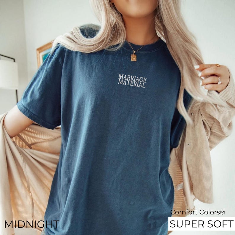 Puede incluir: Una camiseta azul oscuro con el texto "Marriage Material" bordado en blanco. La camiseta est&aacute; etiquetada como "Midnight" y "Comfort Colors&reg; Super Soft".