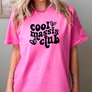 May include: Pink t-shirt with black text that reads "cool massis club" and two hearts.