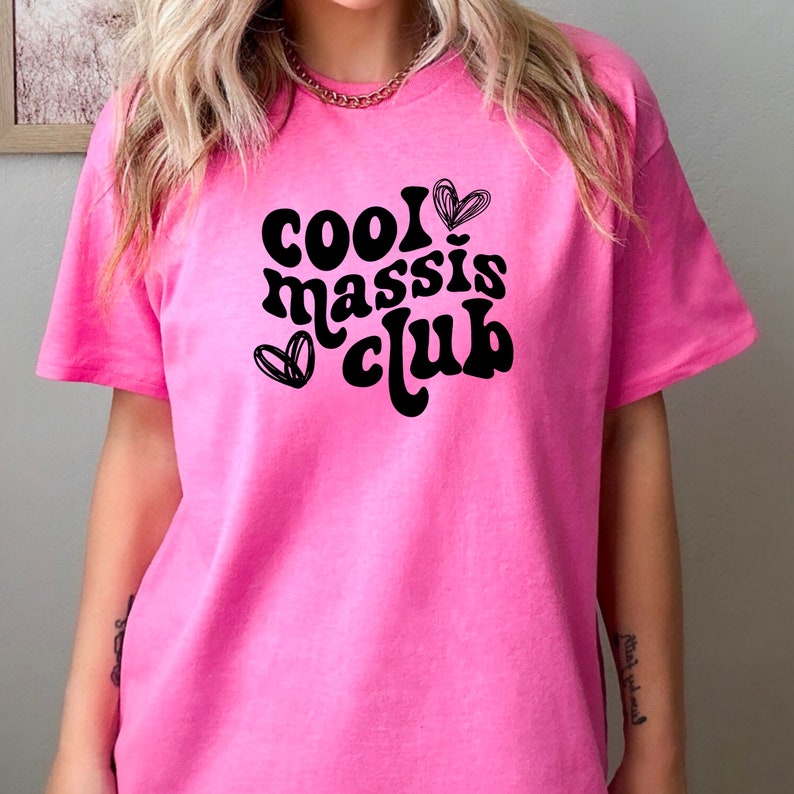May include: Pink t-shirt with black text that reads "cool massis club" and two hearts.