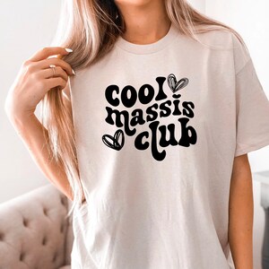 May include: A white t-shirt with black text that reads "cool massis club" with a heart design.