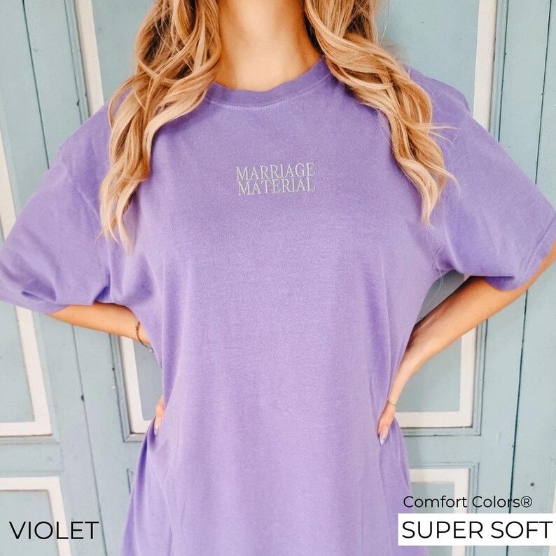 Puede incluir: Una camiseta de manga corta, s&uacute;per suave, de color morado con el texto "Marriage Material" impreso en blanco en la parte delantera.