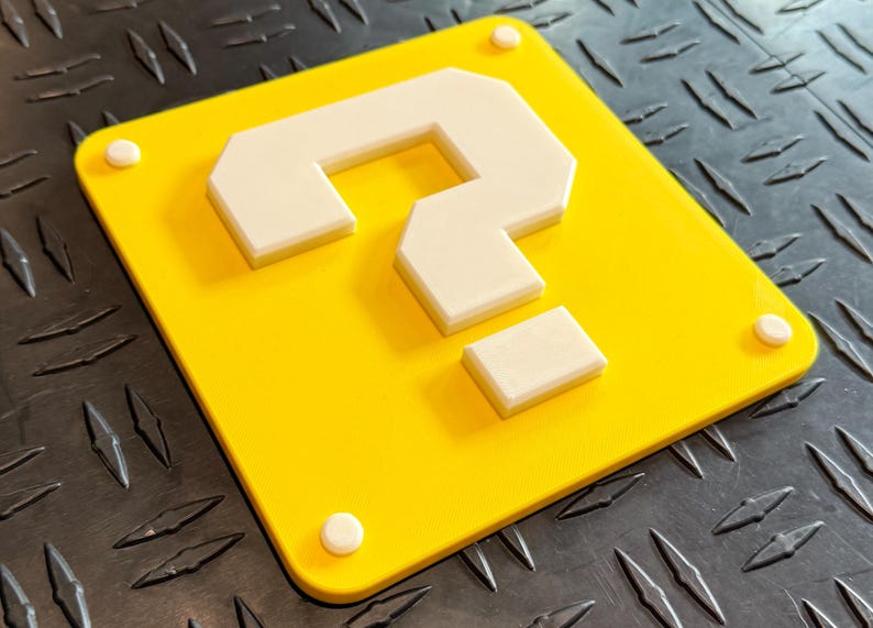 May include: A yellow square with a white question mark in the center. The question mark is made of multiple pieces of white plastic.