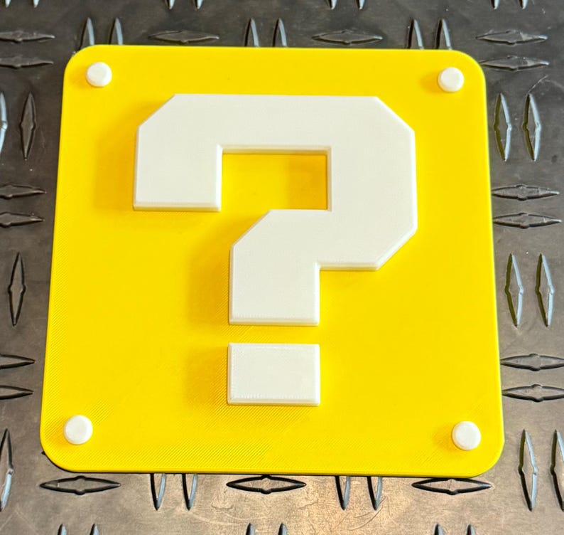 May include: A yellow square with a white question mark in the center. The question mark is made of blocks and has a pixelated look. The square has four white dots on the edges.