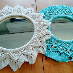 May include: Two macrame mirrors, one white and one turquoise blue, with fringe detailing. Both mirrors have a round shape and are decorated with small white beads.