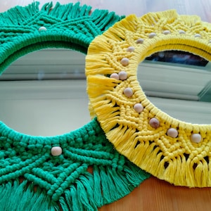 May include: Two round macrame mirrors with wooden beads. The larger mirror is yellow and the smaller mirror is green.