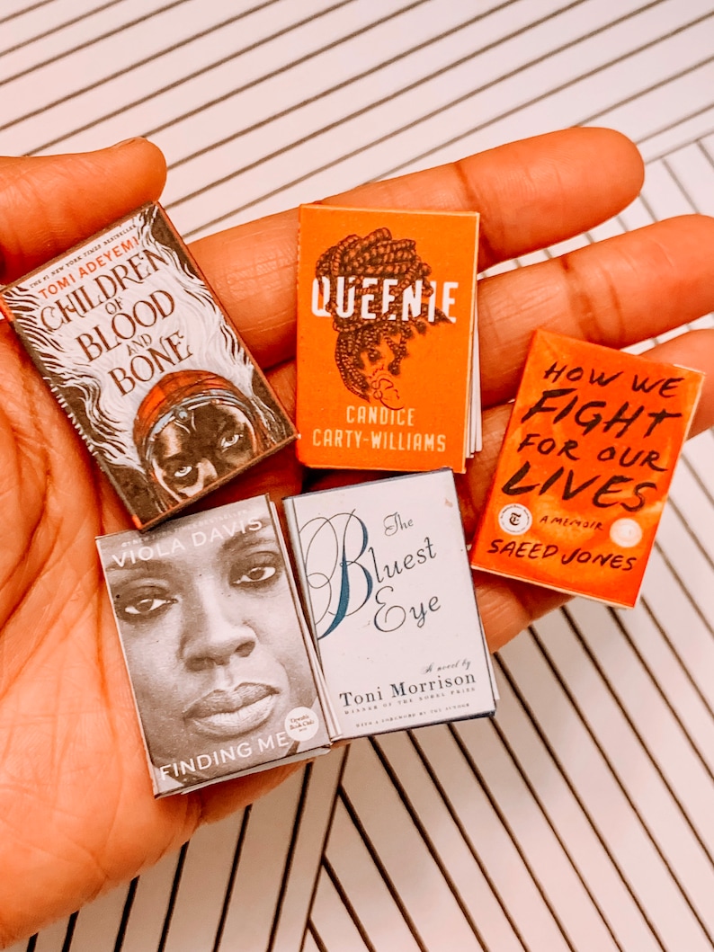 May include: A collection of five paperback books with different titles and authors. The books are all in a similar style, with colourful covers and black text. The titles include "Children of Blood and Bone", "Queenie", "How We Fight for Our Lives", "Finding Me", and "The Bluest Eye".