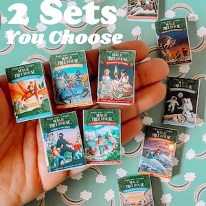 May include: A collection of miniature Magic Tree House books. The books are arranged in a hand, with the covers facing the viewer. The books are all different colors and have different illustrations on the covers. The text on the covers reads "Magic Tree House".