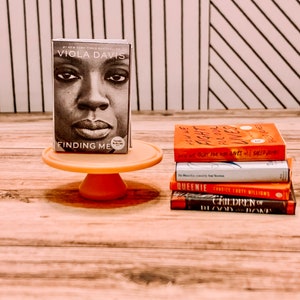May include: A stack of five books on a wooden surface. The top book is titled "Finding Me" by Viola Davis. The other books are titled "How We Fight For Our Lives", "Queenle", "Children of Blood and Bone", and "The Vanishing Half".
