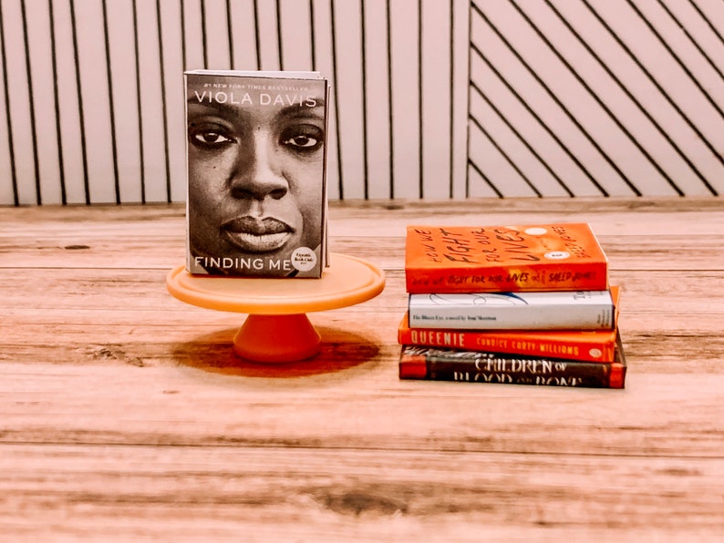May include: A stack of five books on a wooden surface. The top book is titled "Finding Me" by Viola Davis. The other books are titled "How We Fight For Our Lives", "Queenle", "Children of Blood and Bone", and "The Vanishing Half".