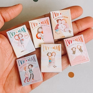 以下が含まれることがあります： 2人の若い女の子のイラストが描かれたカラフルな表紙を持つ、6冊のミニチュアハードカバー本のセットです。本は「Ivy + Bean」というタイトルで、それぞれ異なるタイトルが付けられています。「And the Ghost That Had to Go」、「Break the Fossil Record」、「Take Care of the Babysitter」、「Bound to Be Bad」、「Doomed to Dance」などです。