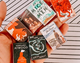 Könnte beinhalten: Eine Sammlung von Miniatur-Taschenbüchern, darunter "Tierfarm", "The Outsiders", "Von Mäusen und Menschen", "Die Früchte des Zorns", "Brave New World", "The Handmaid's Tale" und "Der Fänger im Roggen".