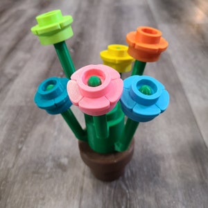 May include: A colorful flower bouquet with green stems and a brown pot. The flowers are made of plastic and have different colors, including pink, blue, yellow, orange, and green.