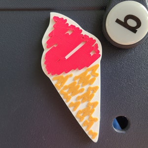 May include: A white ice cream cone with a red ice cream scoop on top. The cone is decorated with a yellow pattern.