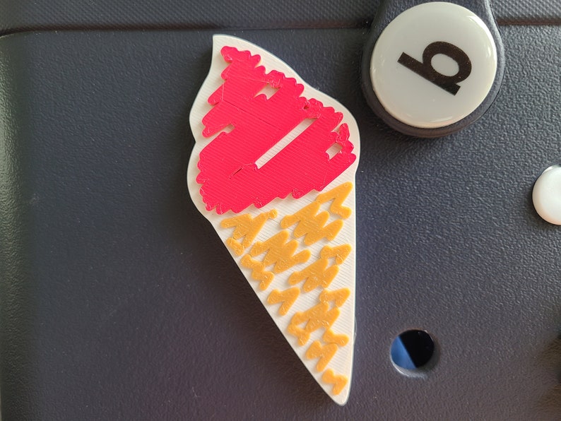 May include: A white ice cream cone with a red ice cream scoop on top. The cone is decorated with a yellow pattern.