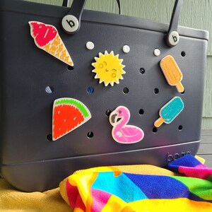 May include: A black tote bag with a variety of colorful, embroidered patches attached to it. The patches include a watermelon, a flamingo, a sun, a popsicle, and an ice cream cone. The bag has the word "boo" printed on the bottom.