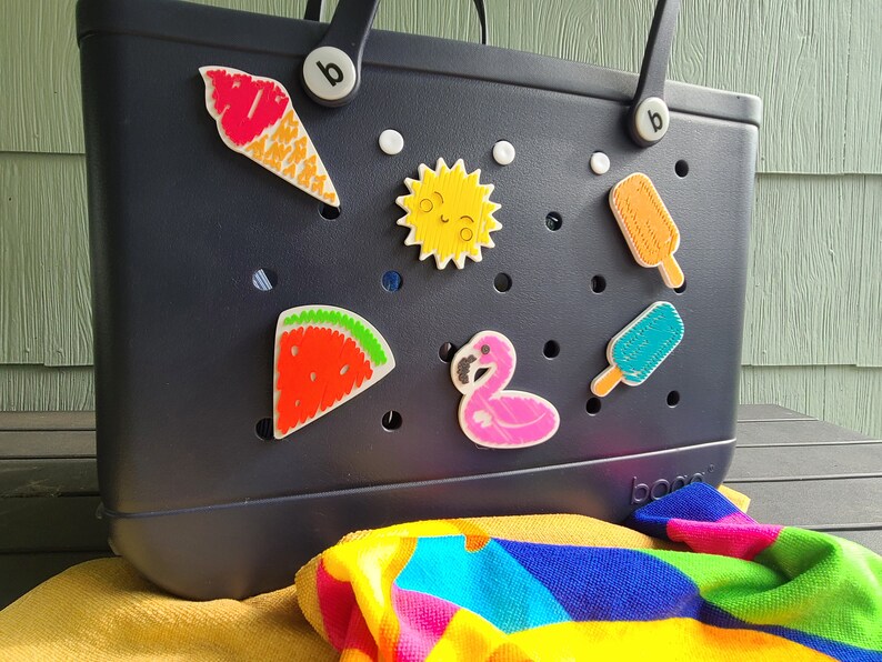 May include: A black tote bag with a variety of colorful, embroidered patches attached to it. The patches include a watermelon, a flamingo, a sun, a popsicle, and an ice cream cone. The bag has the word "boo" printed on the bottom.
