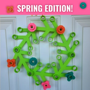 May include: A green wreath made of plastic pipe connectors with colorful flower-shaped pieces attached. The wreath says "SPRING EDITION!" at the top.