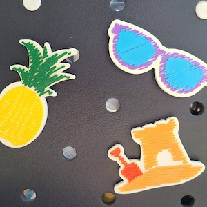 May include: A set of four felt patches featuring a pineapple, sunglasses, a sandcastle, and a bucket and shovel. The patches are all white with colorful details.