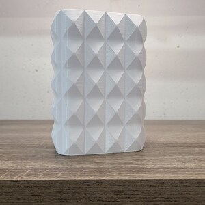 May include: A white, rectangular, three-dimensional object featuring a repeating geometric pattern of raised, pointed diamond shapes across its front surface. The structure has a textured finish with visible horizontal lines.