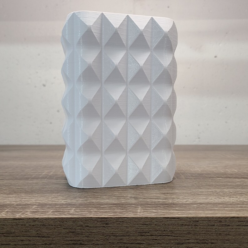 May include: A white, rectangular, three-dimensional object featuring a repeating geometric pattern of raised, pointed diamond shapes across its front surface. The structure has a textured finish with visible horizontal lines.
