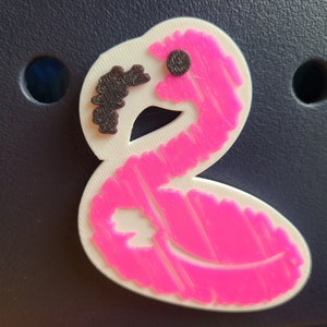 May include: Pink flamingo-shaped charm with a black eye and a textured surface.