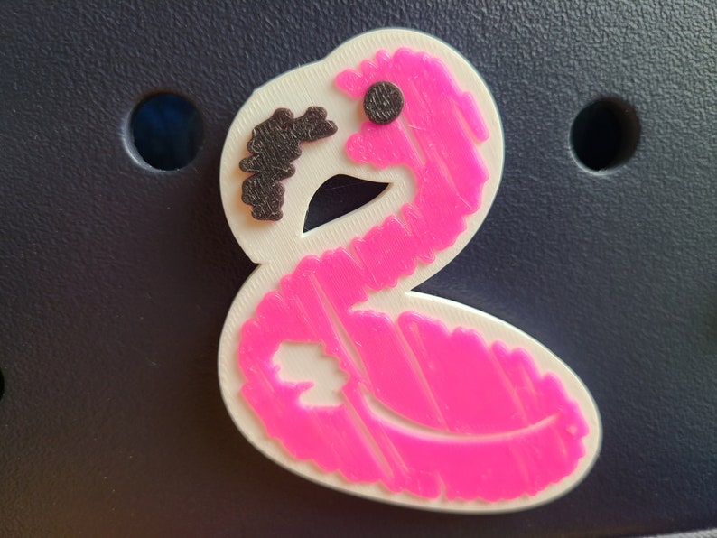 May include: Pink flamingo-shaped charm with a black eye and a textured surface.