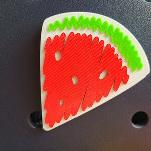 May include: A red and green watermelon-shaped puzzle piece with a white background. The watermelon is made of small, interlocking pieces.