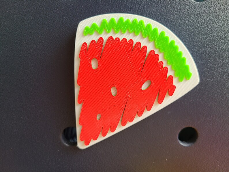 May include: A red and green watermelon-shaped puzzle piece with a white background. The watermelon is made of small, interlocking pieces.