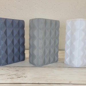May include: Three rectangular containers with a textured, geometric diamond pattern on the exterior. The containers are arranged in a row, featuring a dark blue, a medium gray, and a white color, each with a matte finish and vertical ridges.