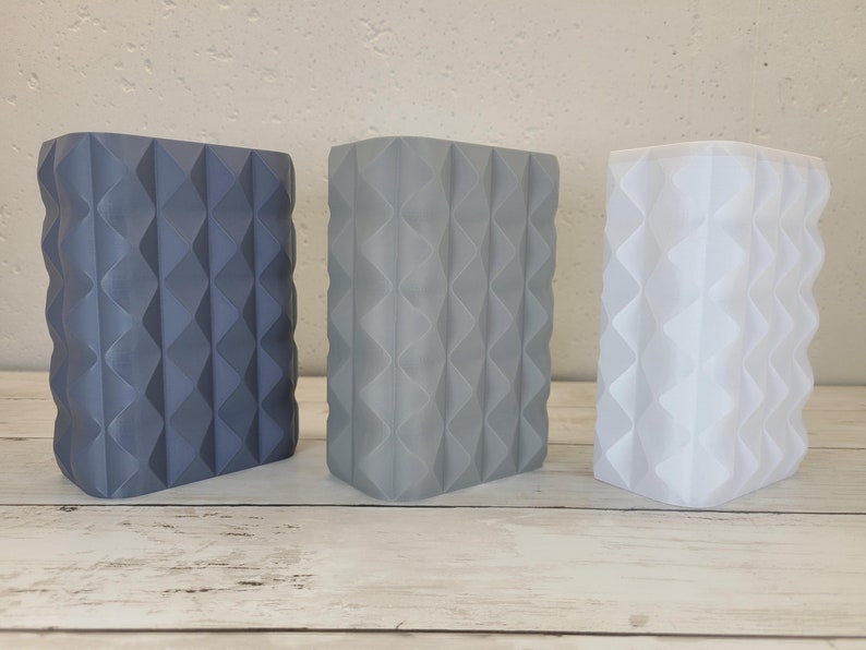 May include: Three rectangular containers with a textured, geometric diamond pattern on the exterior. The containers are arranged in a row, featuring a dark blue, a medium gray, and a white color, each with a matte finish and vertical ridges.