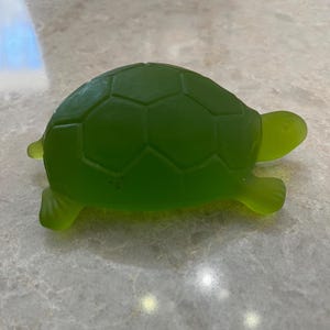 May include: A translucent green turtle figurine. The turtle has a segmented shell and visible legs and head. The figurine is made of a smooth, possibly glass-like material.