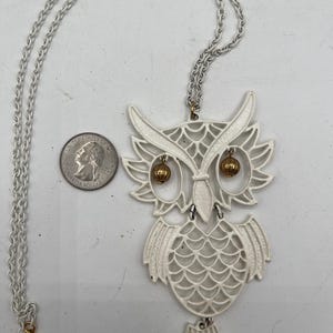 May include: White owl pendant necklace with gold accents. The owl is made of metal and has a detailed design. The necklace is 20 inches long and has a lobster clasp closure.