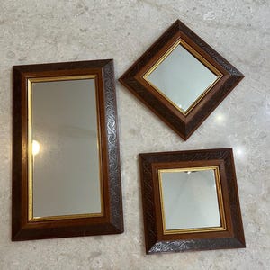 May include: Three decorative mirrors with brown wooden frames. The mirrors are rectangular, square, and diamond-shaped, each with a gold inner frame. The frames feature an embossed floral design.