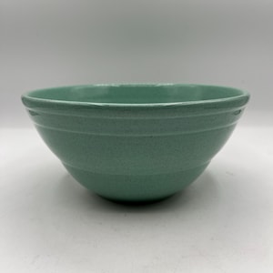 May include: A speckled, light green ceramic mixing bowl. The bowl has a rounded shape with a wide opening and a slightly textured surface. The exterior features three horizontal bands. The bowl is designed for food preparation.