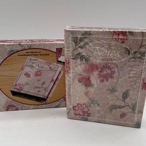 May include: A floral patterned box with the word "Notes" on the front. The box is closed and has a white background with pink and green floral accents. The box is sitting on a white surface. The box comes with 200 sheets of coordinated paper.