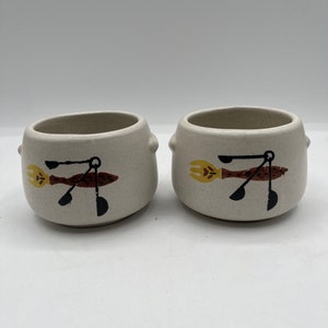 Peut inclure: Deux bols en céramique blanche avec des motifs stylisés brun, noir et jaune d'un ustensile de cuisine avec une flamme à l'extrémité. Les bols ont une surface texturée.