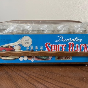 May include: A decorative spice rack with a wooden frame and a blue background. The rack holds several small glass jars, and the packaging includes the text "Decorative Spice Rack" and "Value 9.95".