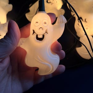 May include: A string of white ghost-shaped Christmas lights with black wires. The ghosts have smiling faces with toothy grins.
