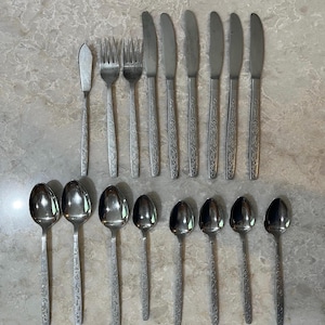 May include: A collection of stainless steel silverware, including forks, knives, spoons, and a butter knife. The silverware has a decorative floral pattern on the handles. The arrangement includes multiple place settings, ideal for a dinner party or special occasion.
