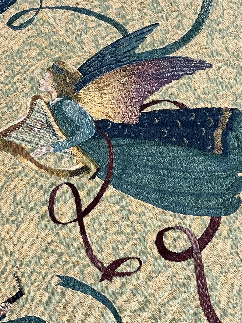 Puede incluir: Primer plano de un tapiz que representa a un &aacute;ngel tocando el arpa. El &aacute;ngel tiene alas azules y moradas y viste de azul. El fondo es un estampado floral en tonos beige y verde. Cintas burdeos y turquesas a&ntilde;aden movimiento.