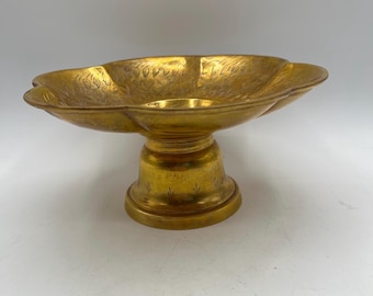May include: A gold-colored metal bowl with a decorative design sits on a matching pedestal. The bowl has a scalloped edge and the pedestal has a round base.